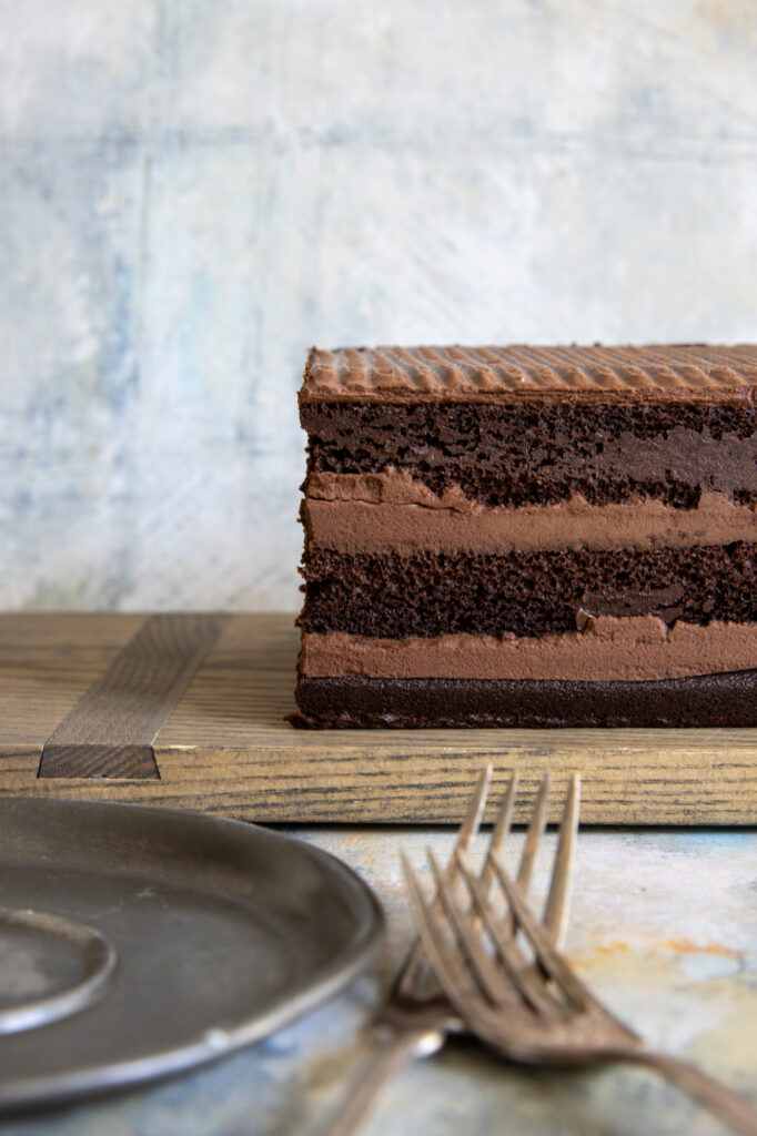 Chocolate fudge layered cake on cutting board with forks.