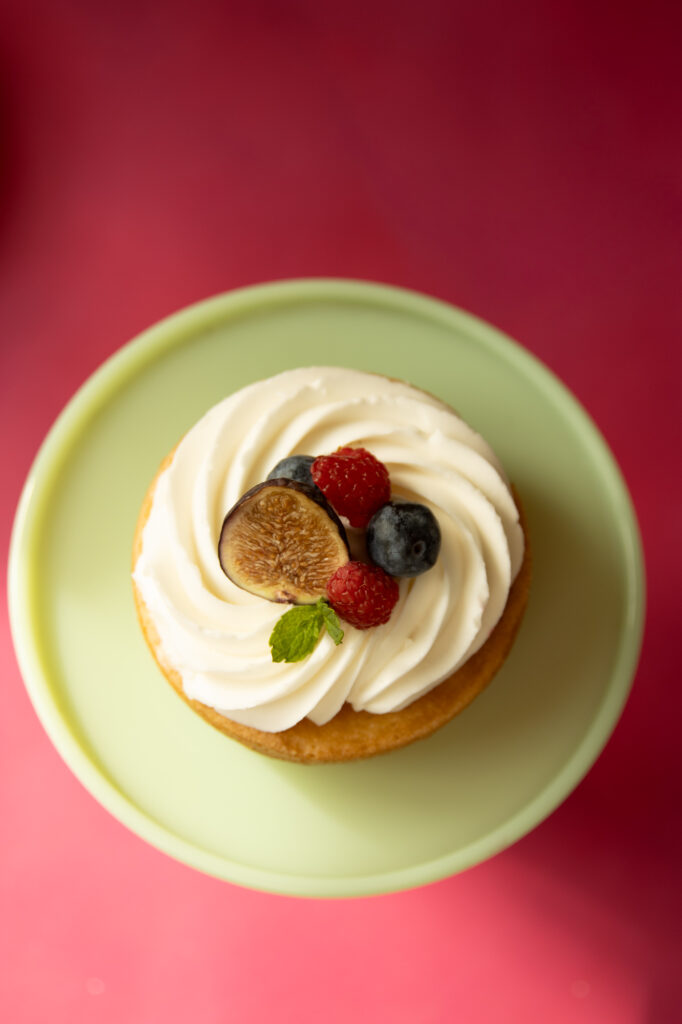 Lemon cake with white frosting and berry topping on green cake stand.